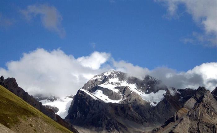 The peak of Om Parvat partly wreathed in cloud above a green slope